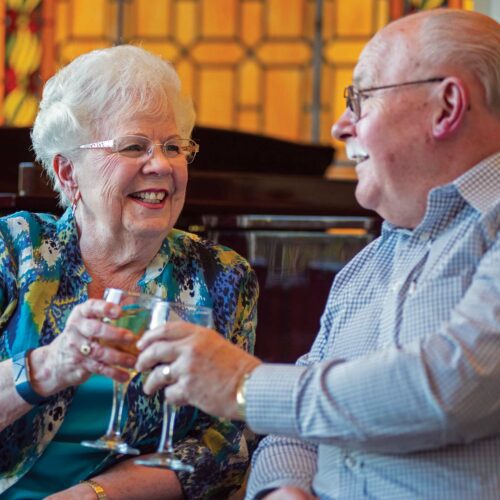 Two residents of the Acacia Creek retirement community toast their drink. For seniors, social connection is the key to successful aging.